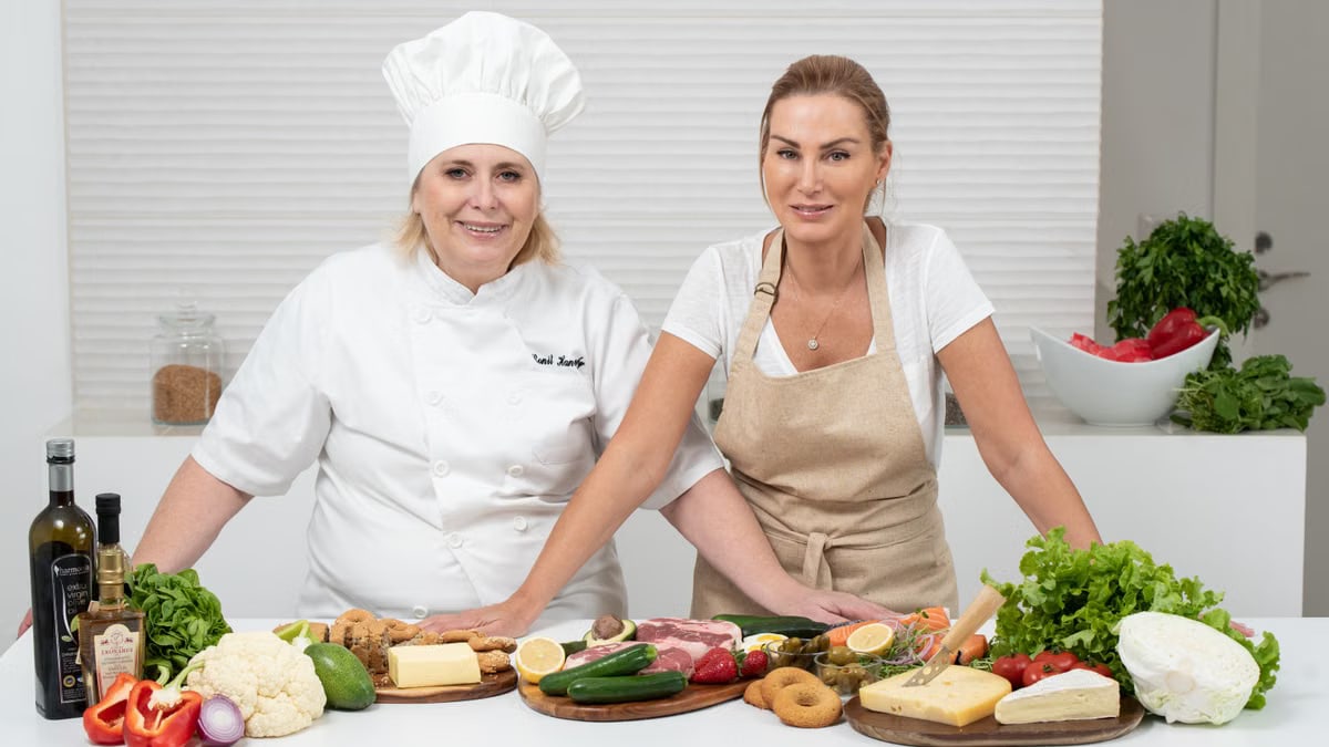 Two female chefs with variety of fresh ingredients in a kitchen setting, showcasing culinary preparation.